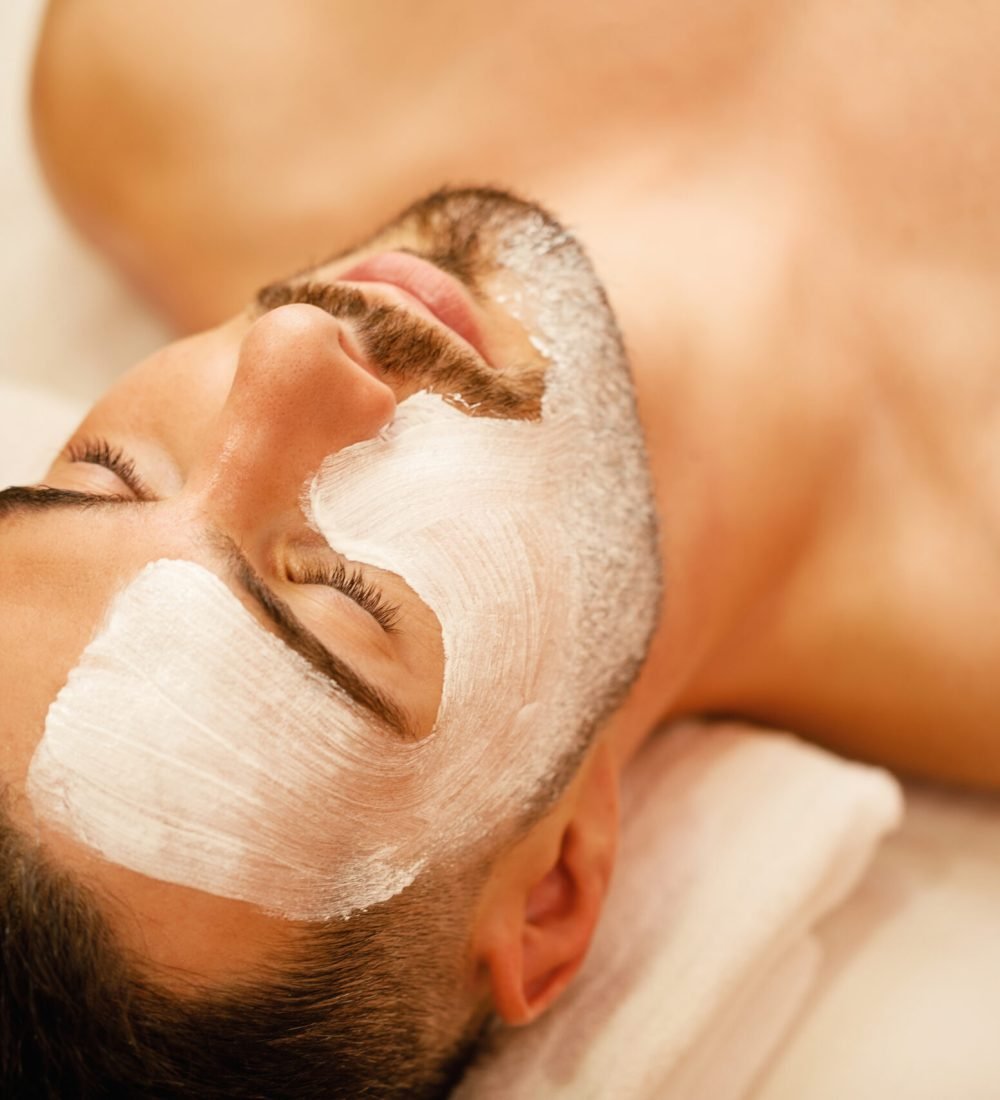Close-up of man with white facial mask relaxing during treatment at beauty spa.
